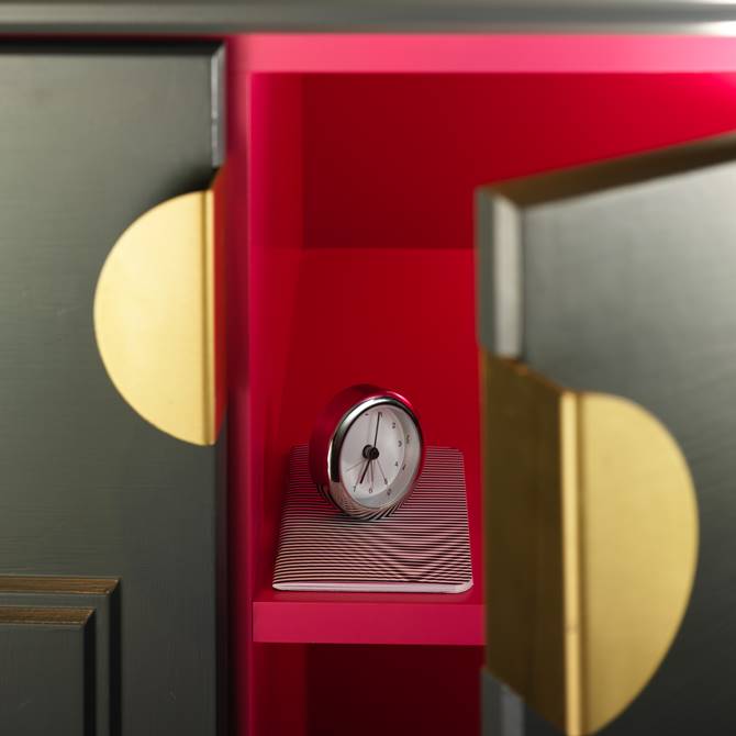 A clock displayed on a shelf within a pink and gold cabinet, showcasing elegant design and color contrast.