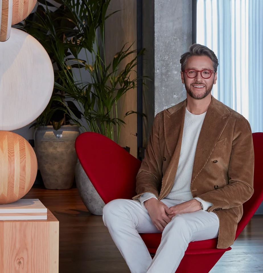 Professional photo of Jacu Strauss sitting in a red armchair with plants in the background.