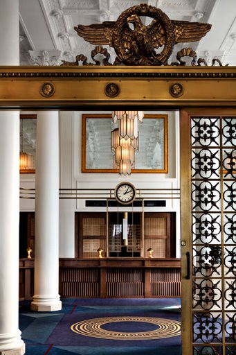Classic hotel reception with a vintage-style clock, wooden counter, and ornate light fixtures, welcoming guests in style.