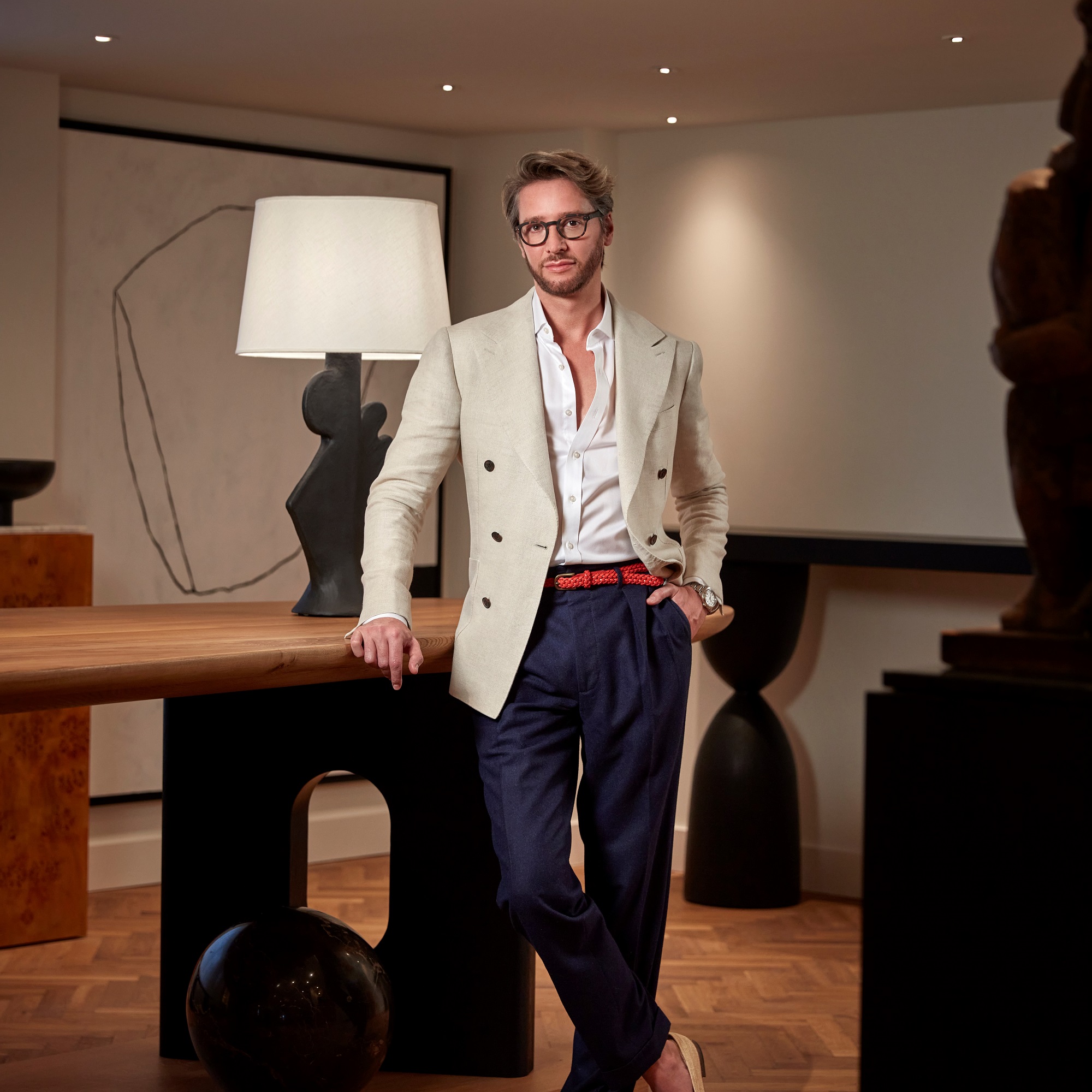 Jacu Strauss at Lyle DC in blazer leans on a sculptural table under soft lighting in a modern room.