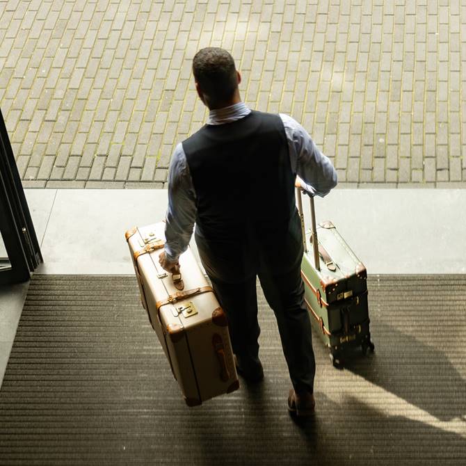Man with two vintage suitcases walking out of a building entrance.