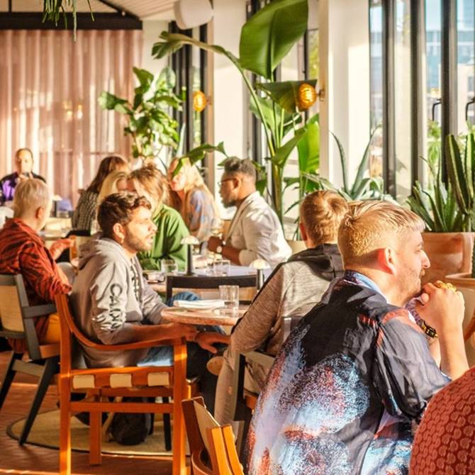 Indoor rooftop bar area at One Hundred Shoreditch in London with people chatting and enjoying the sunshine.