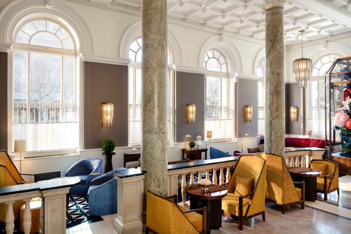 Elegant hotel lounge featuring tall marble columns, large arched windows, and luxurious seating in a bright, airy space.