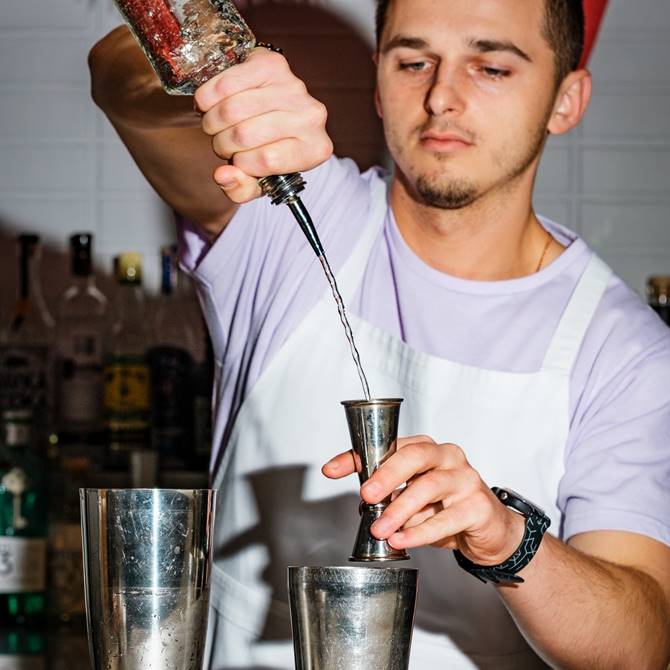 A man skillfully pours a vibrant cocktail into a shaker, preparing for a refreshing drink.