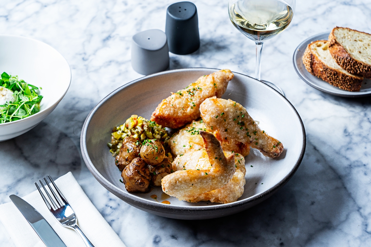 Delicious plated dish at The Lyle, showcasing crispy fried chicken with a side of roasted potatoes and garnish.
