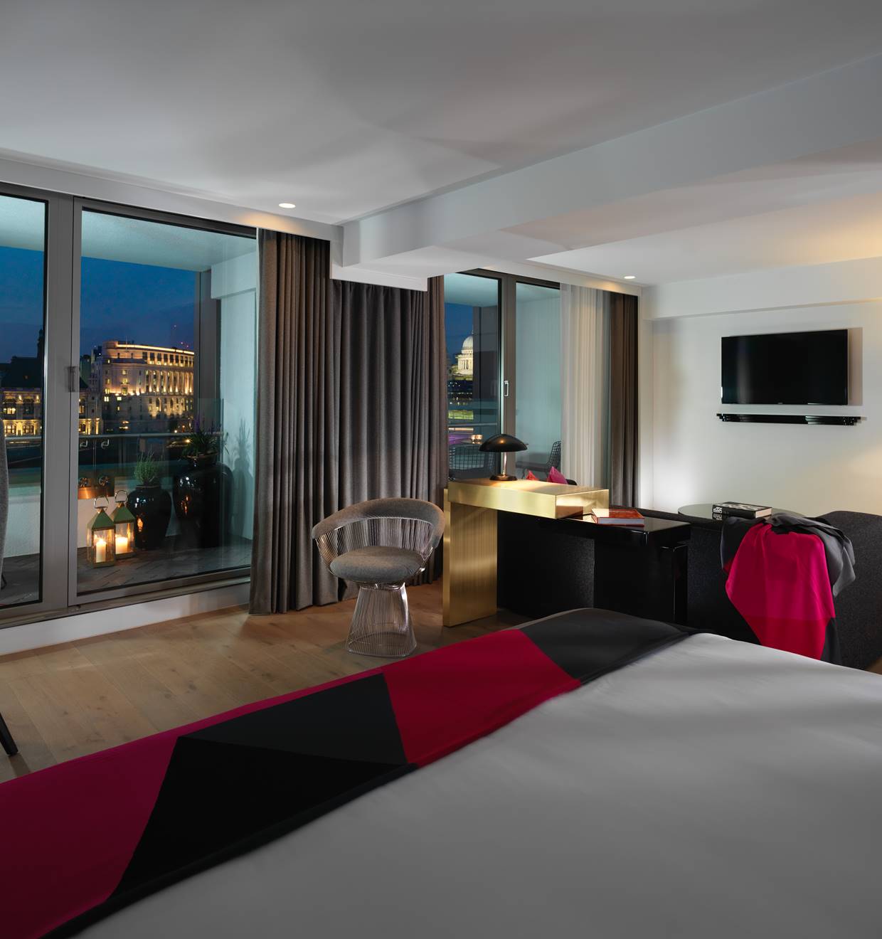A luxurious hotel suite with a balcony offering a stunning river view, featuring modern decor.