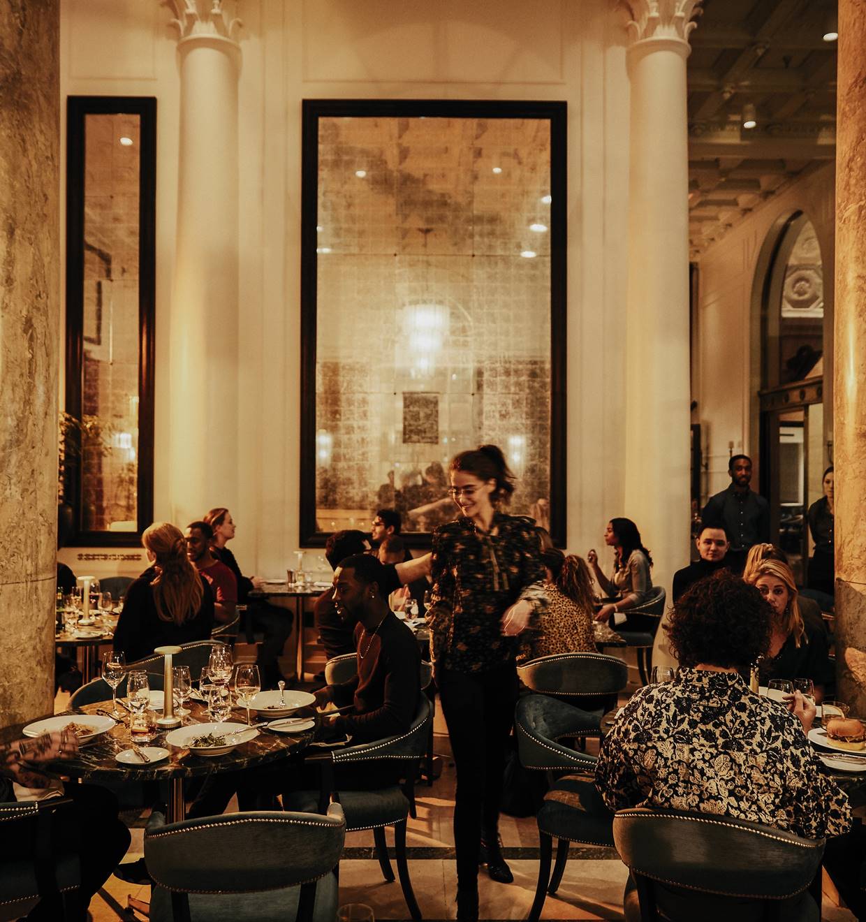 A bustling restaurant scene featuring people seated at tables, surrounded by elegant pillars enhancing the ambiance.