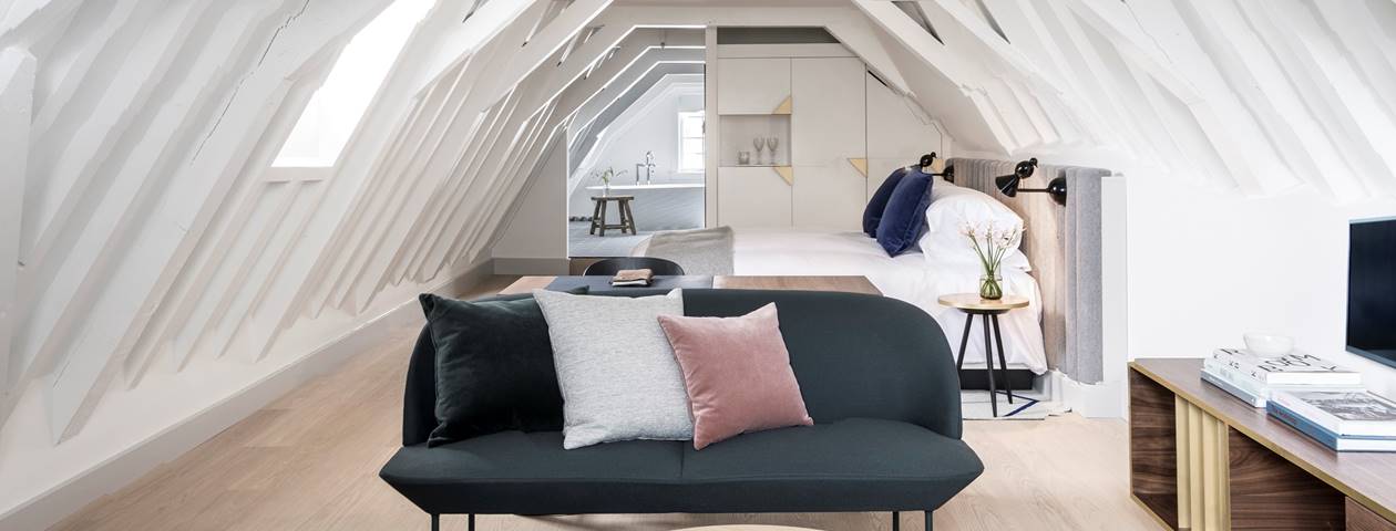 A spacious hotel room with a king-sized bed, modern furnishings, and large windows.