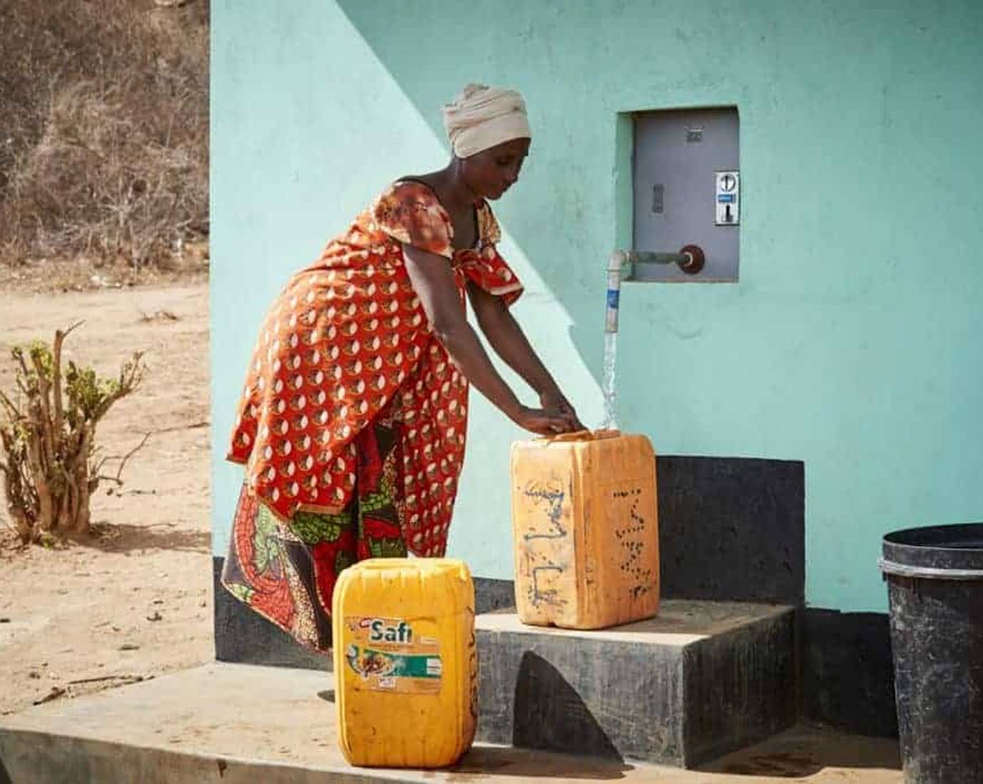 Woman is filling up tanks with fresh water by a building.