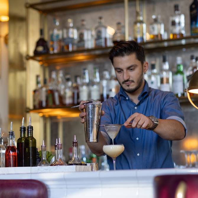 A bartender creates a cocktail at a bar, highlighting the art of mixology in a lively and engaging setting.