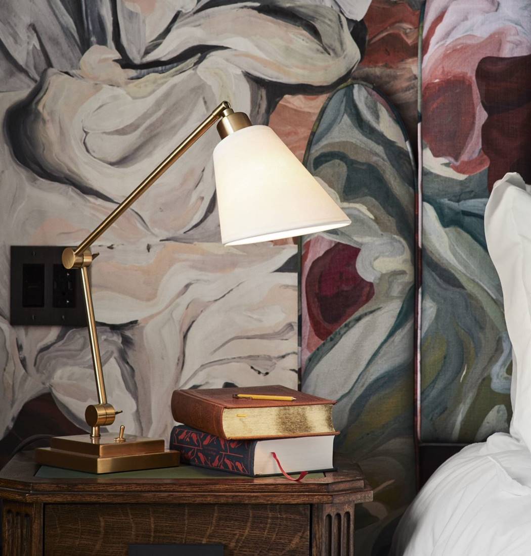 Nightstand with a classic lamp and books by a colorful wallpaper in a hotel room at Riggs DC.