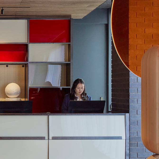 A woman stands at the hotel front desk, assisting guests with check-in and inquiries in a welcoming environment.