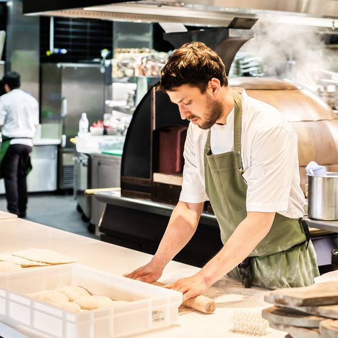 Chef working in a modern kitchen, carefully preparing dough on a countertop, surrounded by professional kitchen equipment.