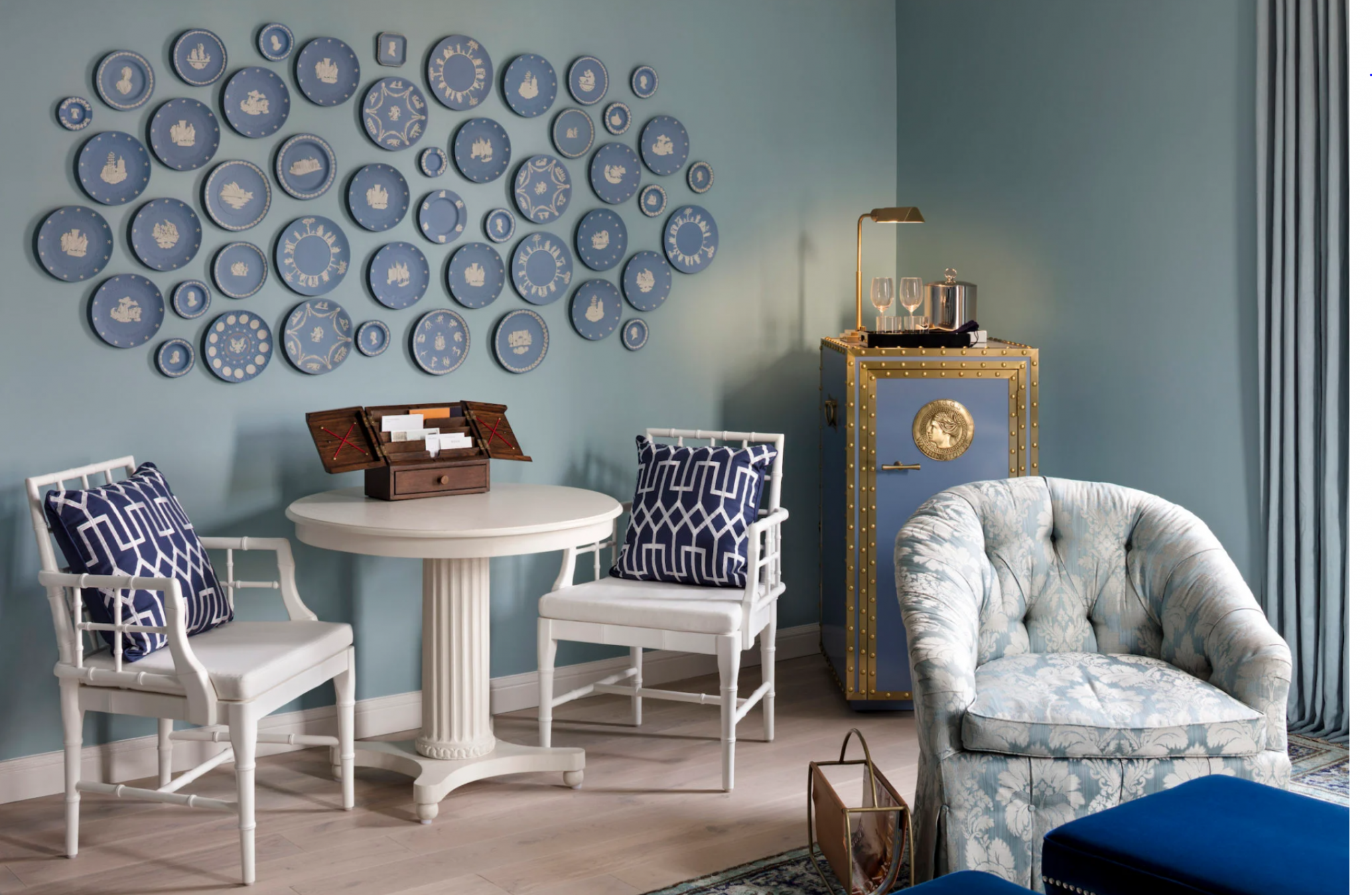 Luxurious hotel suite featuring elegant pink decor, with velvet chairs, draped curtains, and a vintage-style rug.