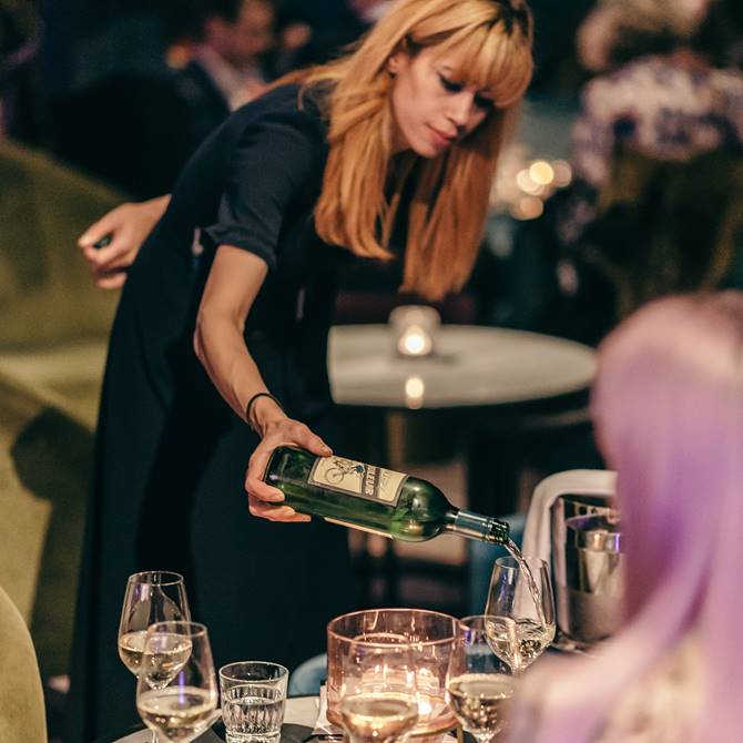 An upscale event with a waitress pouring wine into elegant glasses in a stylish bar area.