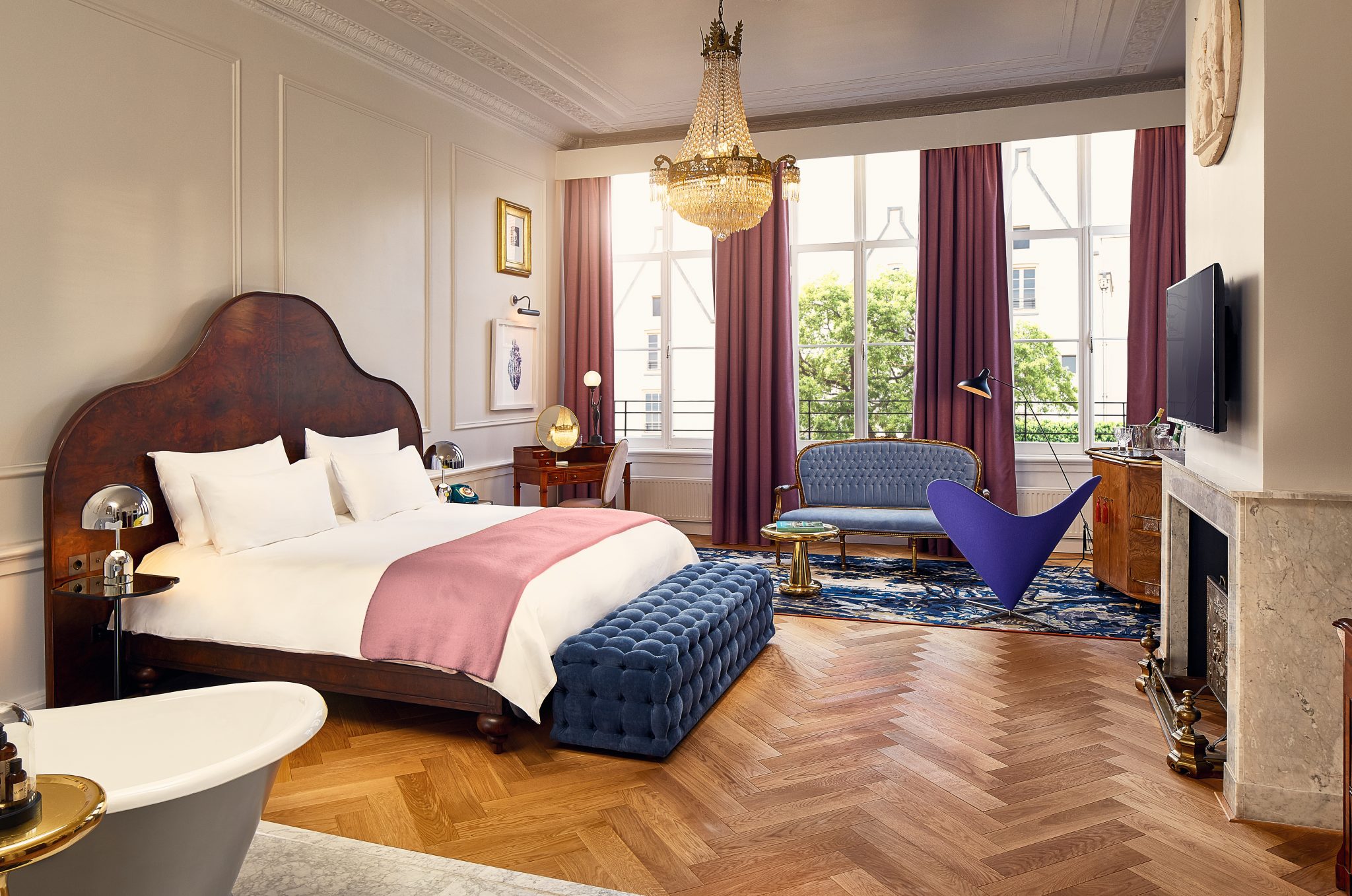 Luxurious hotel suite with a grand chandelier, plush bed, and stylish furnishings at Pulitzer Amsterdam.