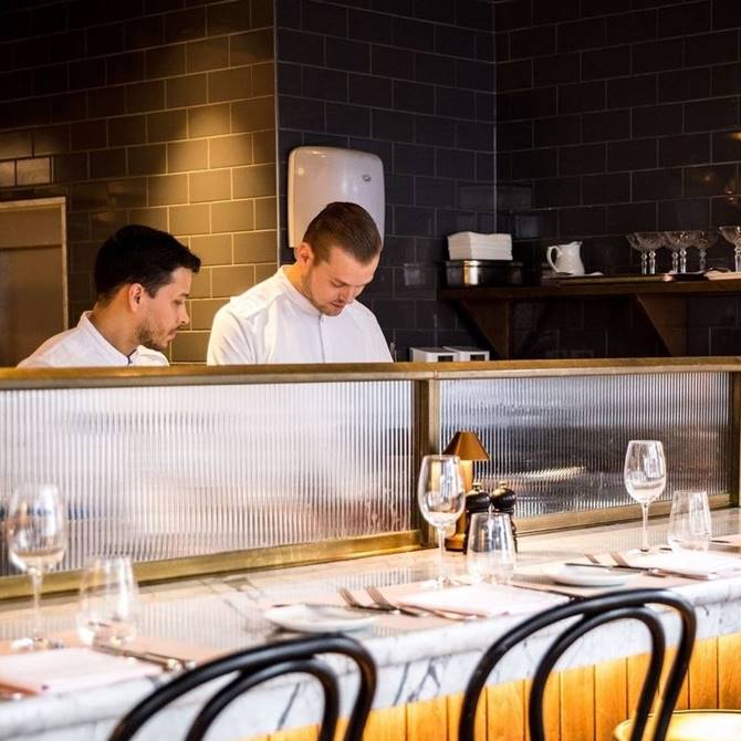 Two chefs collaborate in a bustling restaurant kitchen, preparing dishes with focus and precision.