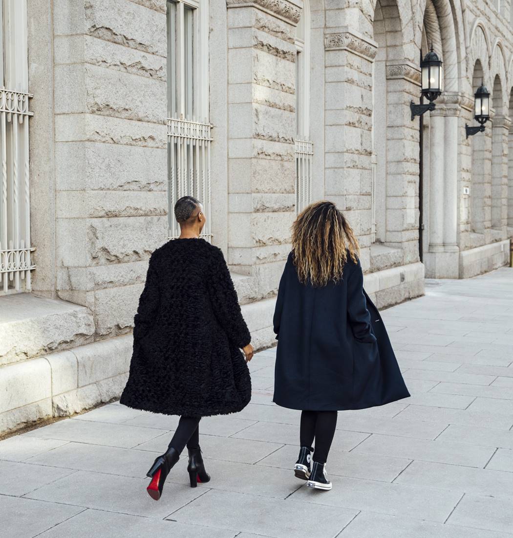 Two well-dressed women walking in the street next to a beautiful traditional building.