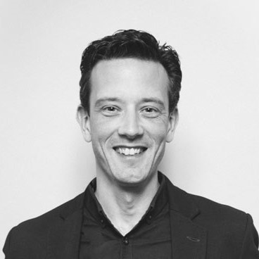 Black and white portrait of a smiling man in a dark blazer.