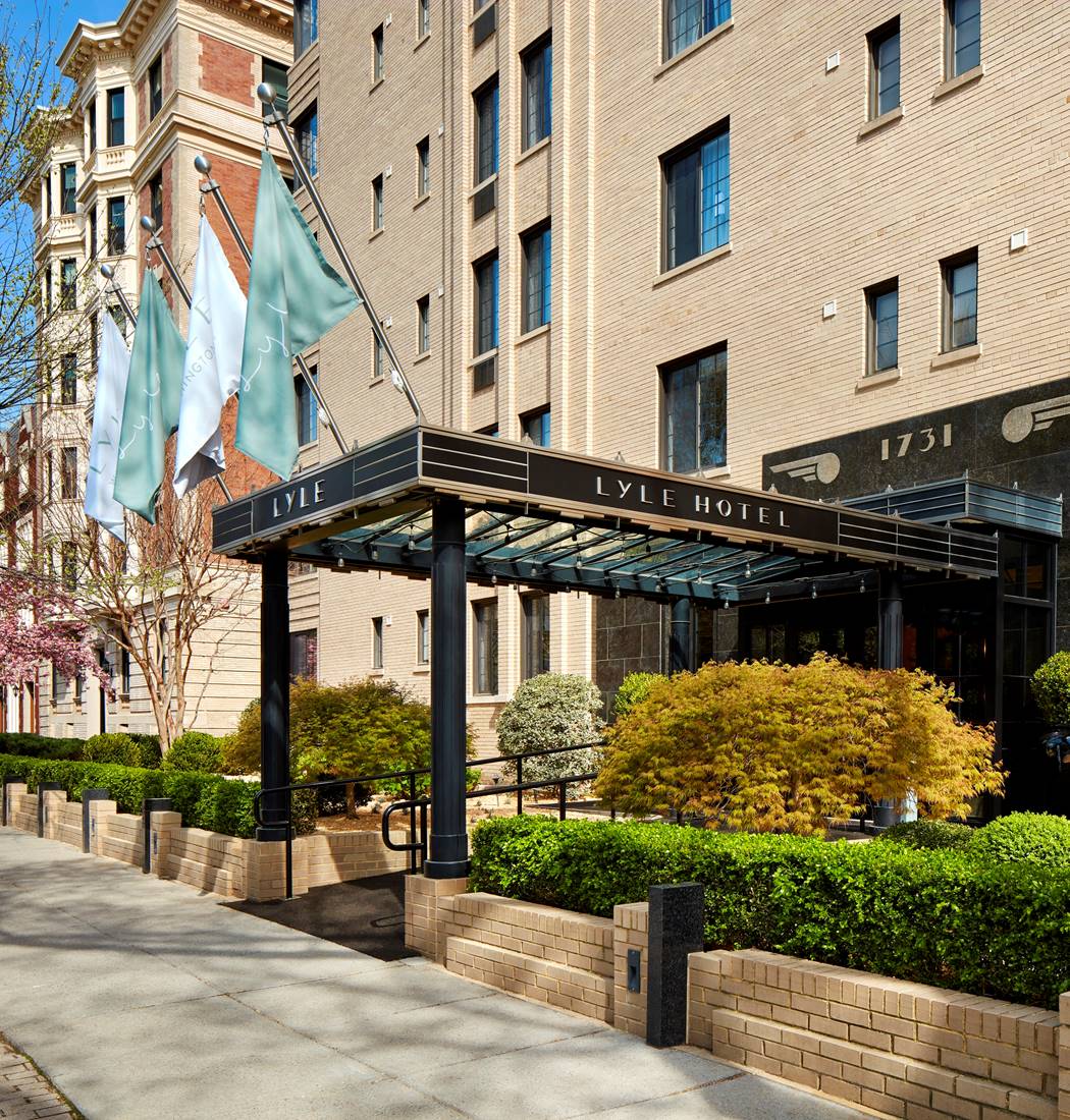 Iconic exterior of the Lyle DC hotel in Washington DC with green bushes and trees blossoming.