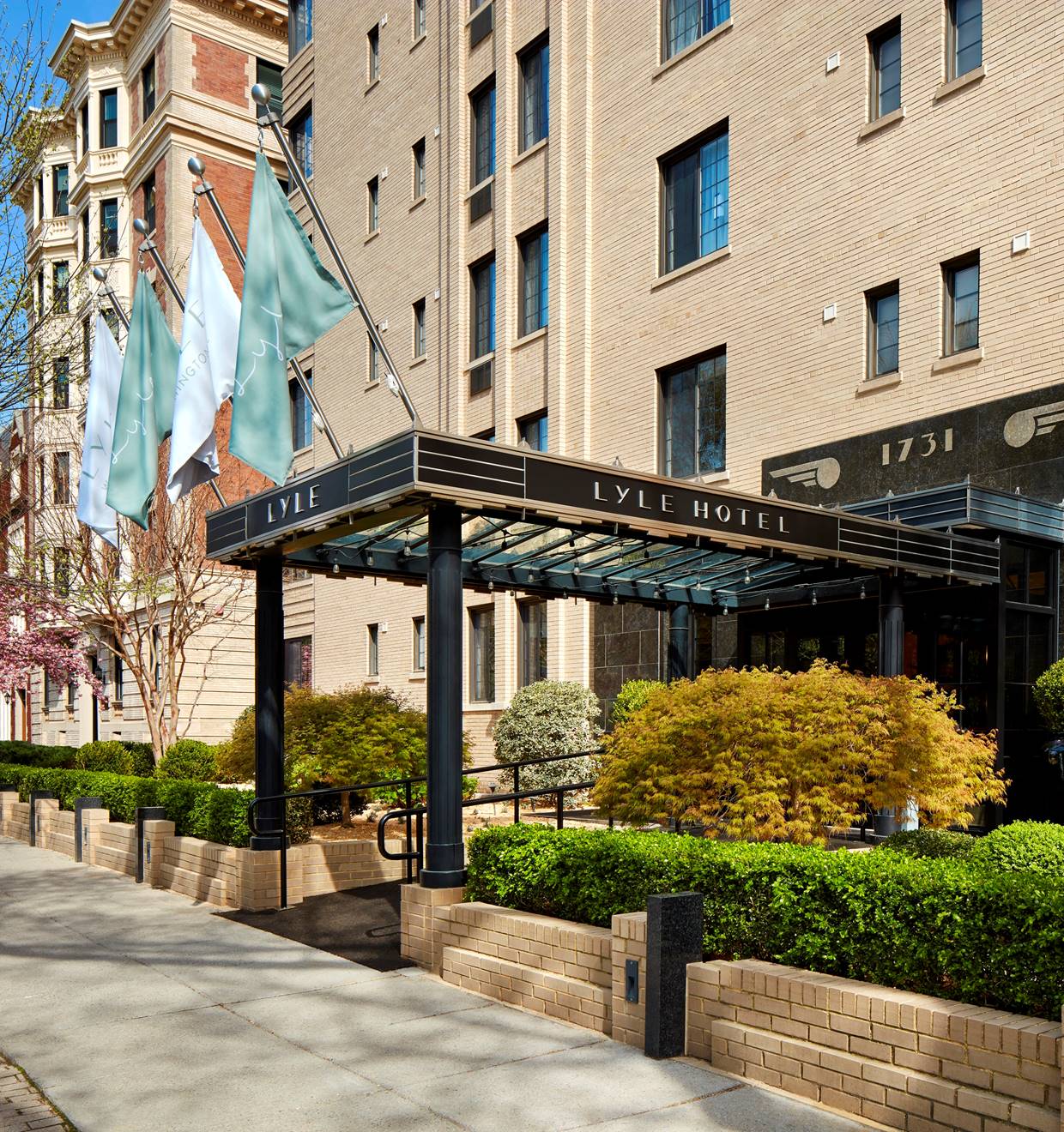 Iconic exterior of the Lyle DC hotel in Washington DC with green bushes and trees blossoming.