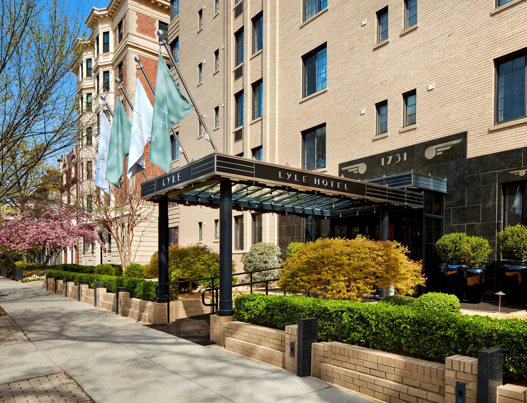 Iconic exterior of the Lyle DC hotel in Washington DC with green bushes and trees blossoming.