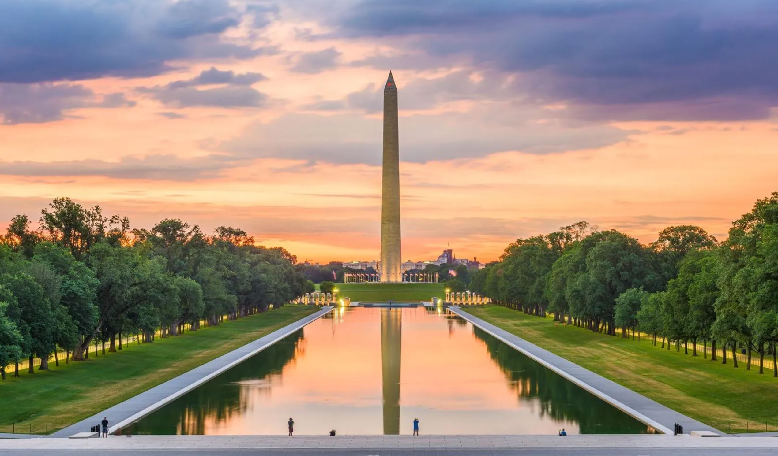 The Washington Monument silhouetted against a vibrant sunset sky, casting a serene reflection on the surrounding landscape.