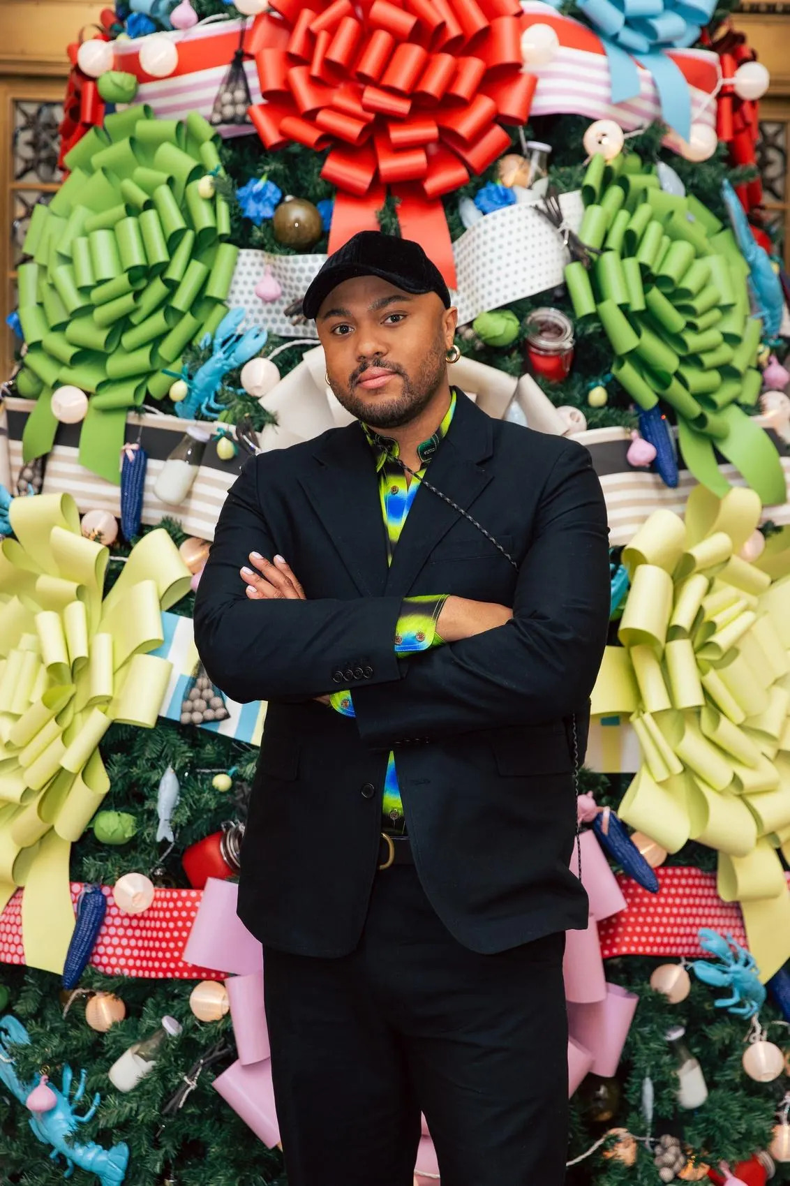 Person in a suit standing confidently in front of a festive bow-filled holiday display.