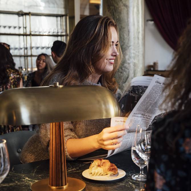 A woman is enjoying her breakfast at the modern and stylish Cafe Riggs in DC with a newspaper in her hand.