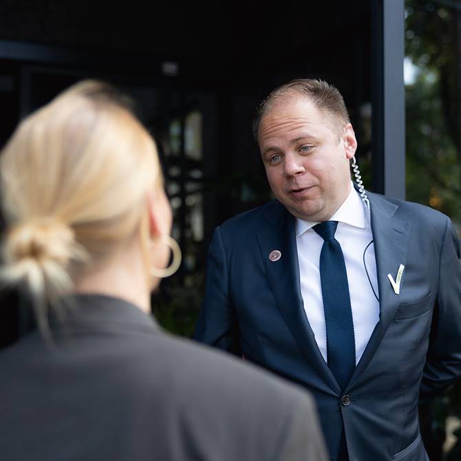 Security staff in a suit talking to a woman outside a building.