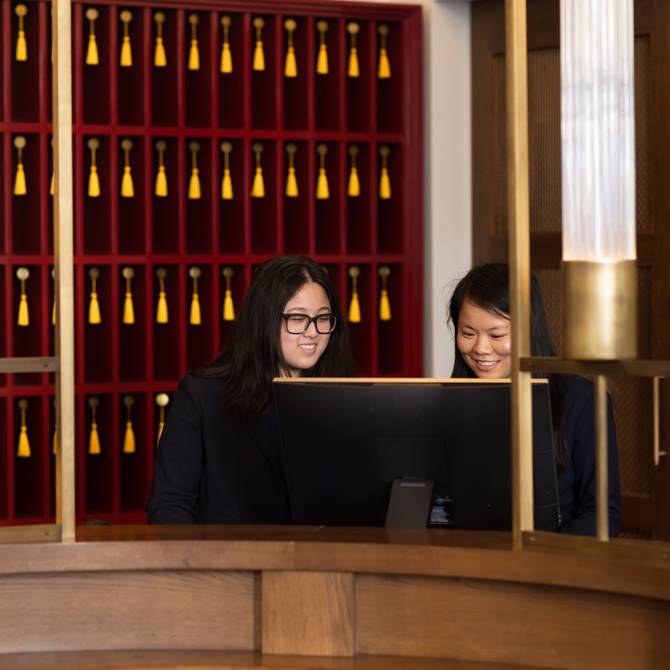 Two women collaborating in front of a computer in a hotel setting, engaged in a productive discussion.