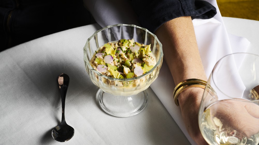 Gourmet dish served in a glass bowl, featuring fresh ingredients like avocado and radish, presented on a white tablecloth.