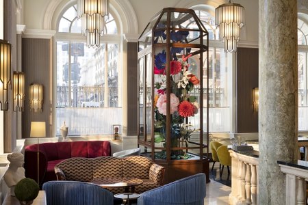 Elegant hotel lobby featuring plush seating, floral arrangements, and tall arched windows letting in natural light.