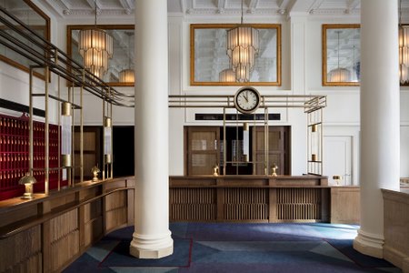 Classic hotel reception with a vintage-style clock, wooden counter, and ornate light fixtures, welcoming guests in style.