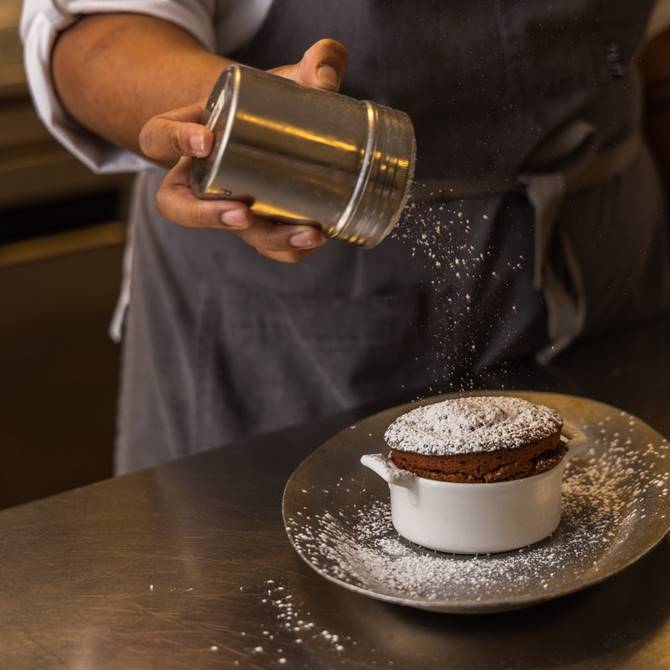 A chef adds a finishing touch of powdered sugar to a dessert, creating an elegant and inviting presentation.