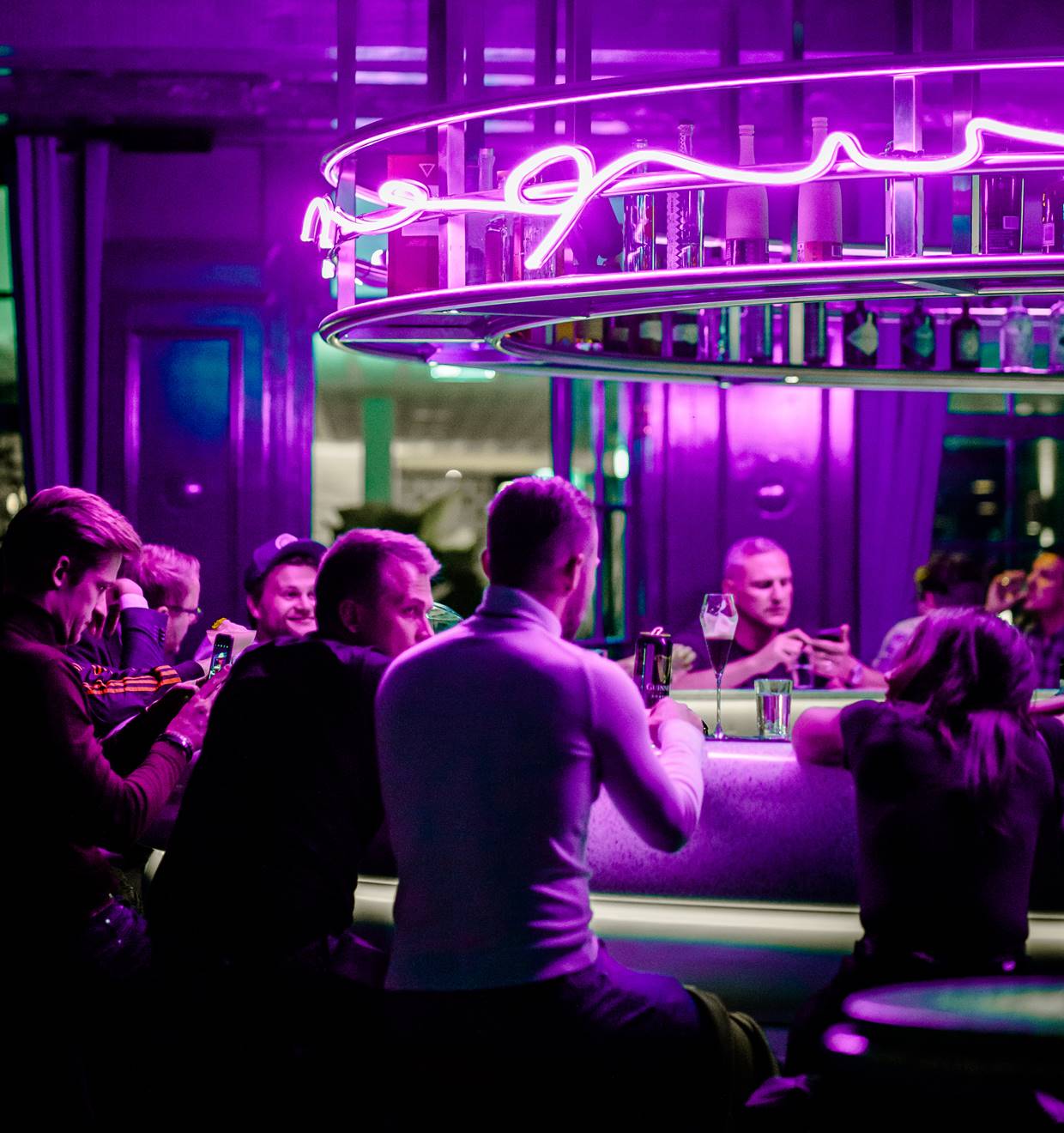 People socialising at a bar illuminated by vibrant purple neon lights, creating a lively night-time atmosphere.