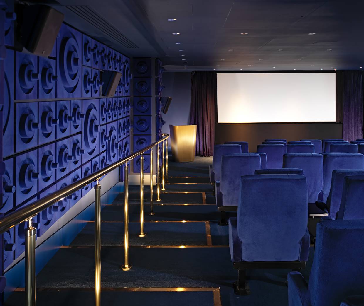 Modern cinema room with plush blue seating, golden railings, and a large projection screen, ready for an exclusive screening.