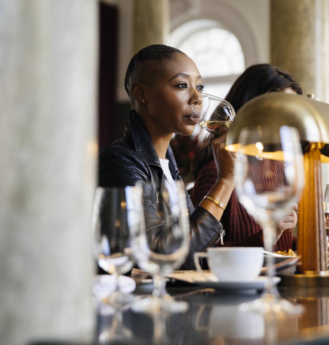 Chic interior at Cafe Riggs with a woman sipping white wine in a modern setting with stylish design and marble columns.