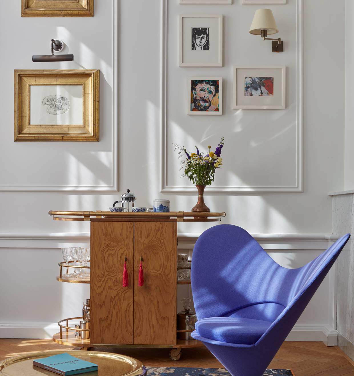 A blue chair positioned in front of a wall adorned with various pictures, creating a cozy and artistic atmosphere.