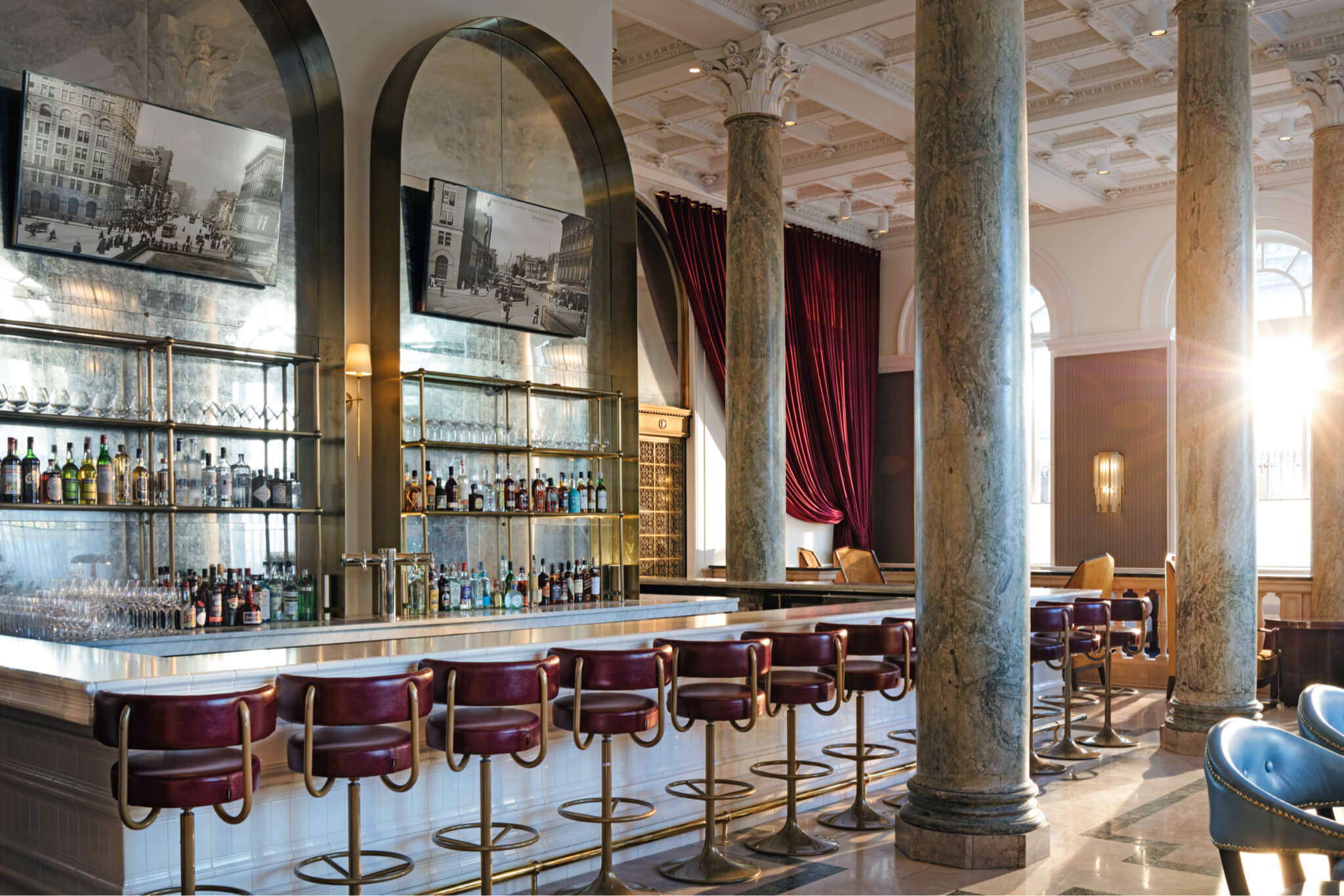 Stylish hotel bar with a long counter, leather stools, and elegant columns, creating a luxurious and classic ambiance.