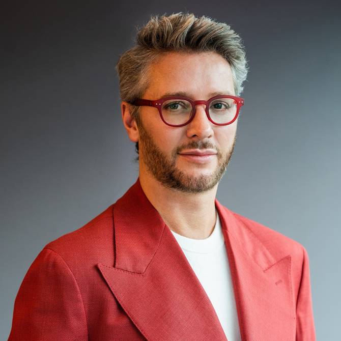Professional shot of Lore Group designer Jacu Strauss in a stylish red suit with red glasses.