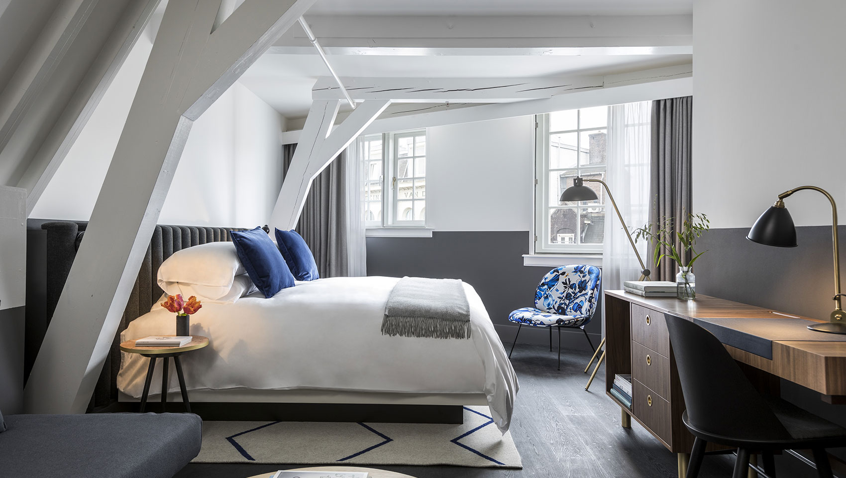 Modern hotel room with exposed wooden beams, a cozy bed, and a mix of contemporary and classic decor elements.